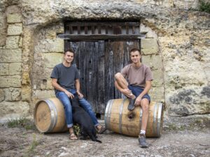 Guillaume e Baptiste dell'azienda vitivinicola Clos Thierriere seduti su damigiane di vino.